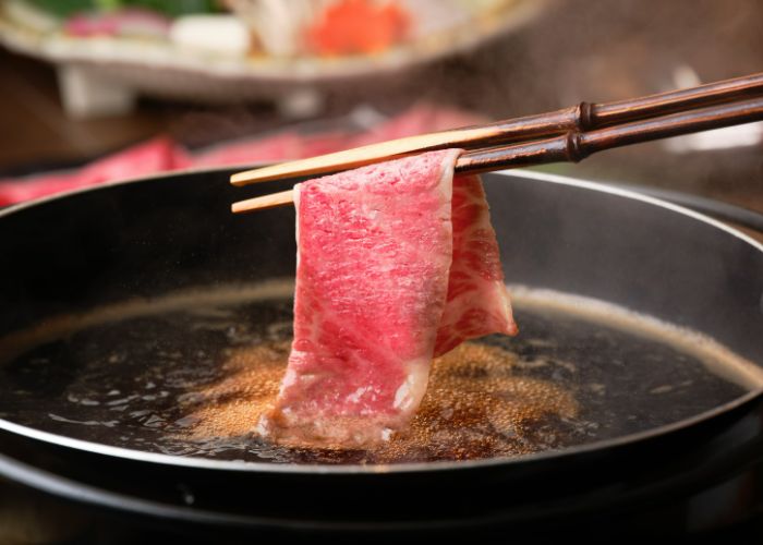 Chopsticks dunking a thin slice of meat onto a grill at the shabu shabu restaurant in Tenzan Tojikyo Onsen.